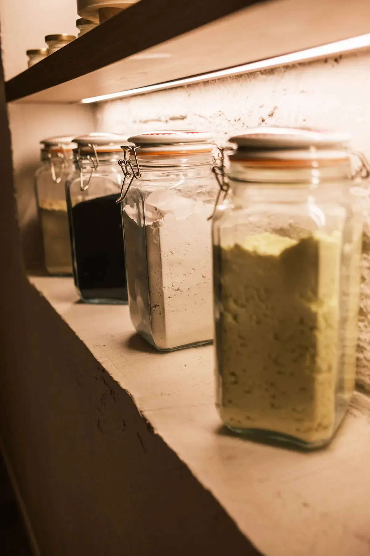 Glass jars of salts and treatment clays on a lit shelf