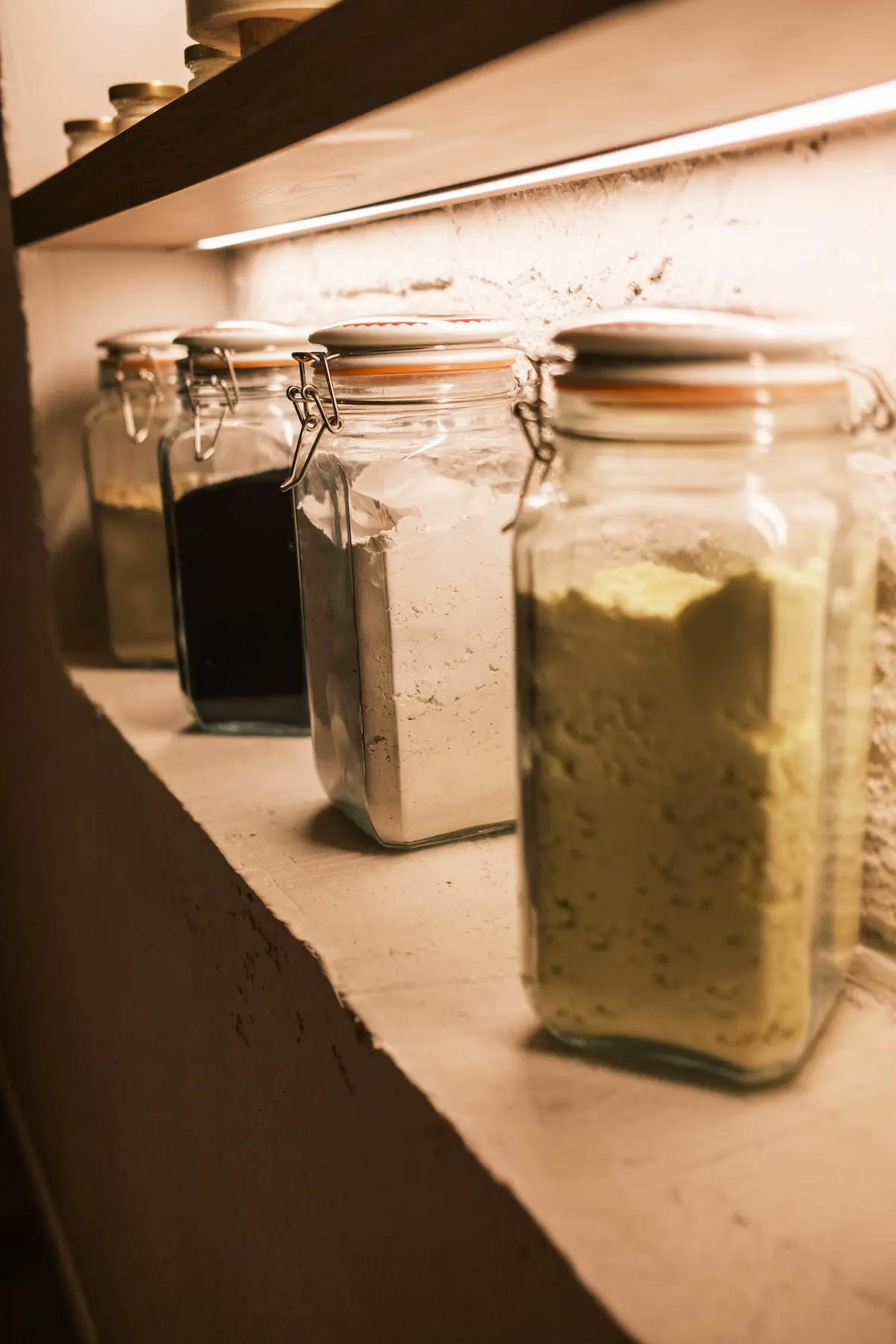 Glass jars of salts and treatment clays on a lit shelf