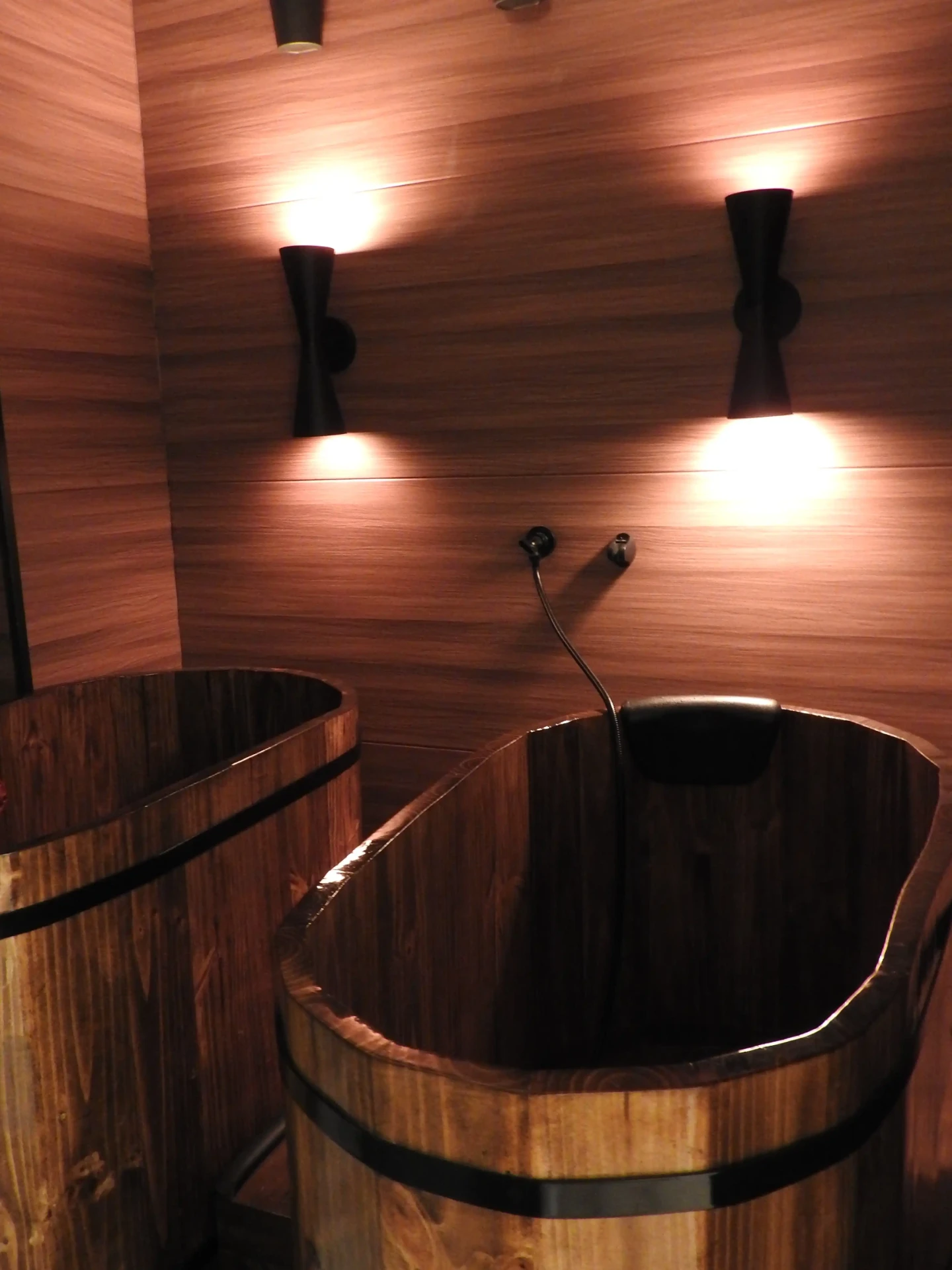 Wooden hot mineral bath tubs under warm sconce lighting